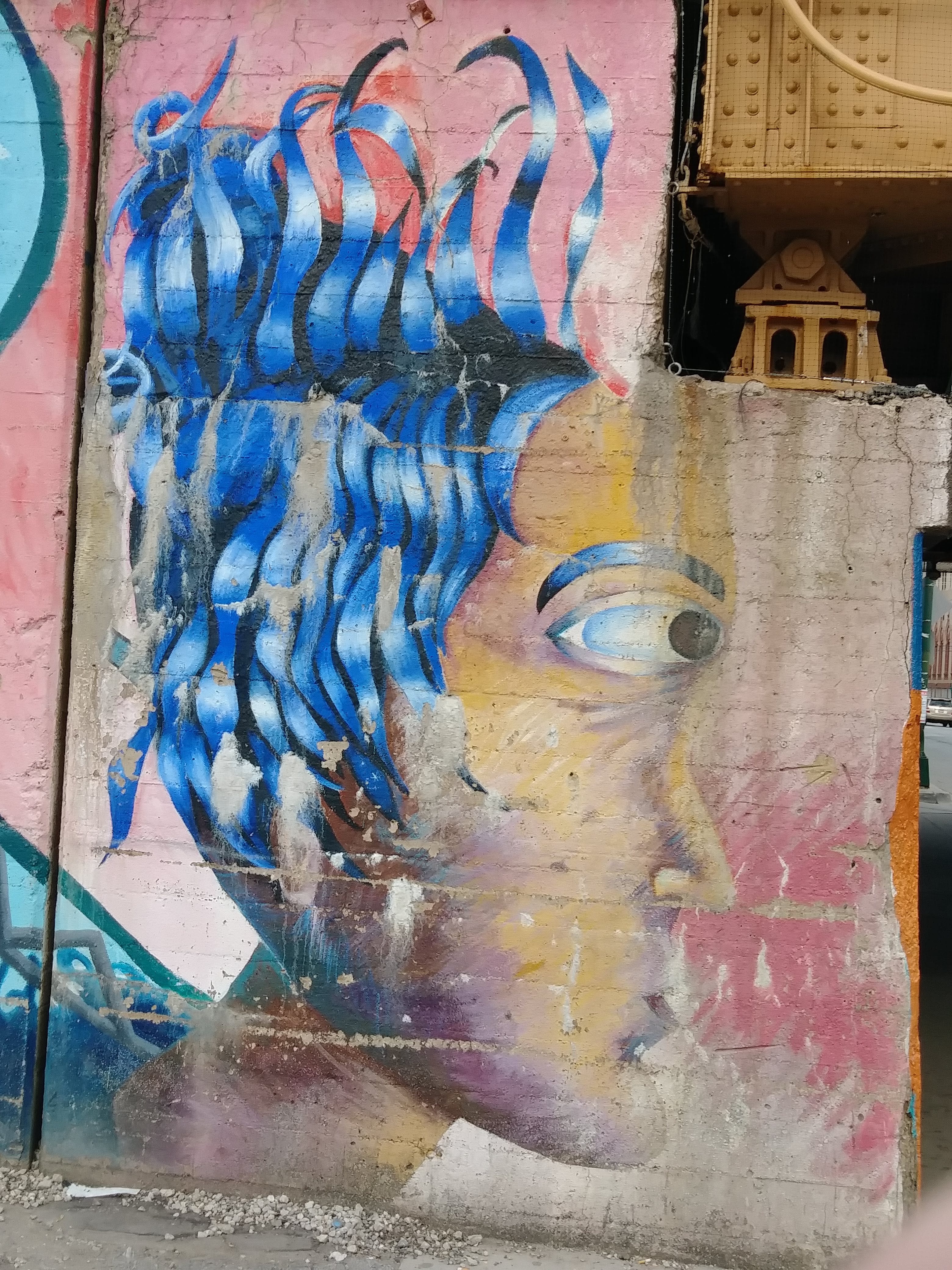 Street art of a person with blue ribbons  for hair in silhouette on a viaduct wall