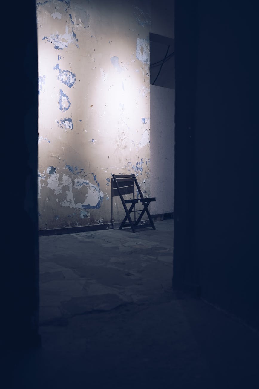 Stock photo of an empty chair, through a door,of a barren room, with a peeling paint wall from Pexels.com