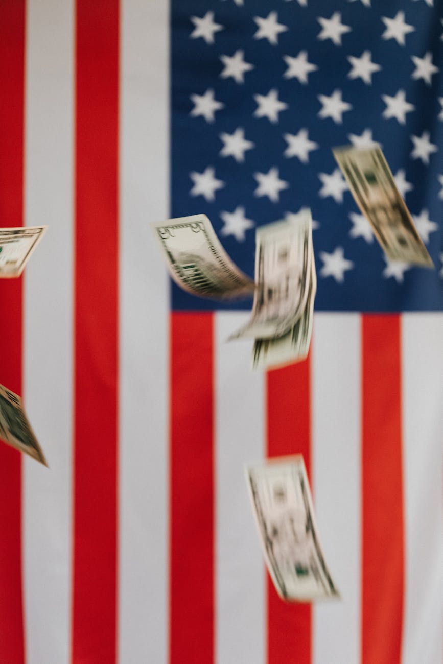 Stock photo of cash floating past United States of America flag from Pexels.com