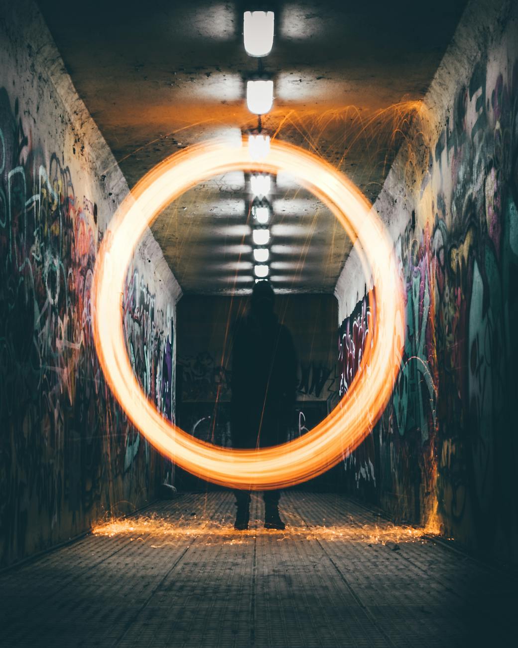 Stock photo of a gold circle framed in fire around a lone figure standing in a hallway with graffiti painted walls from Pexels.com