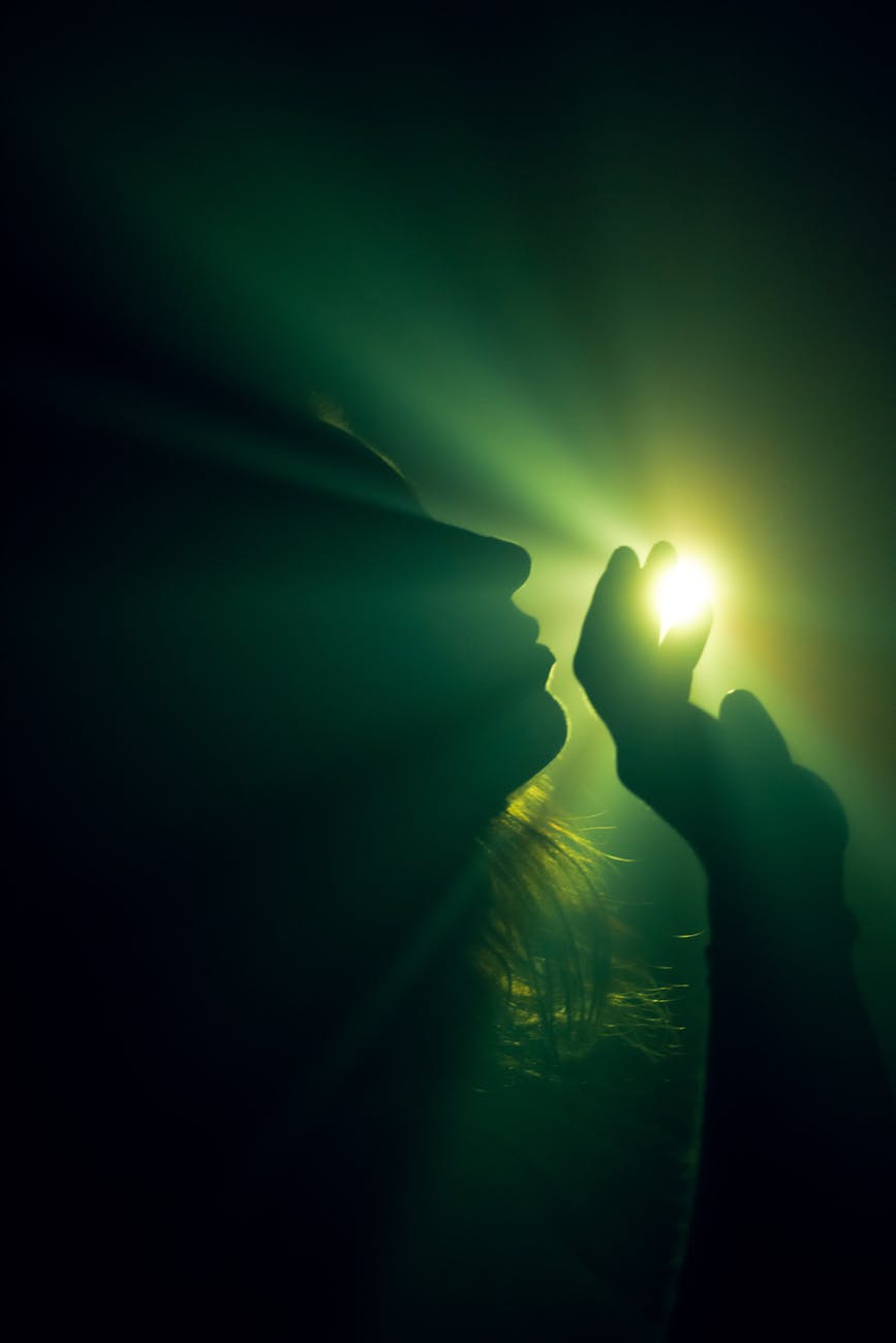 Stock photo of a human profile with upraised hand revealing a green glow through fingers from Pexels.com 