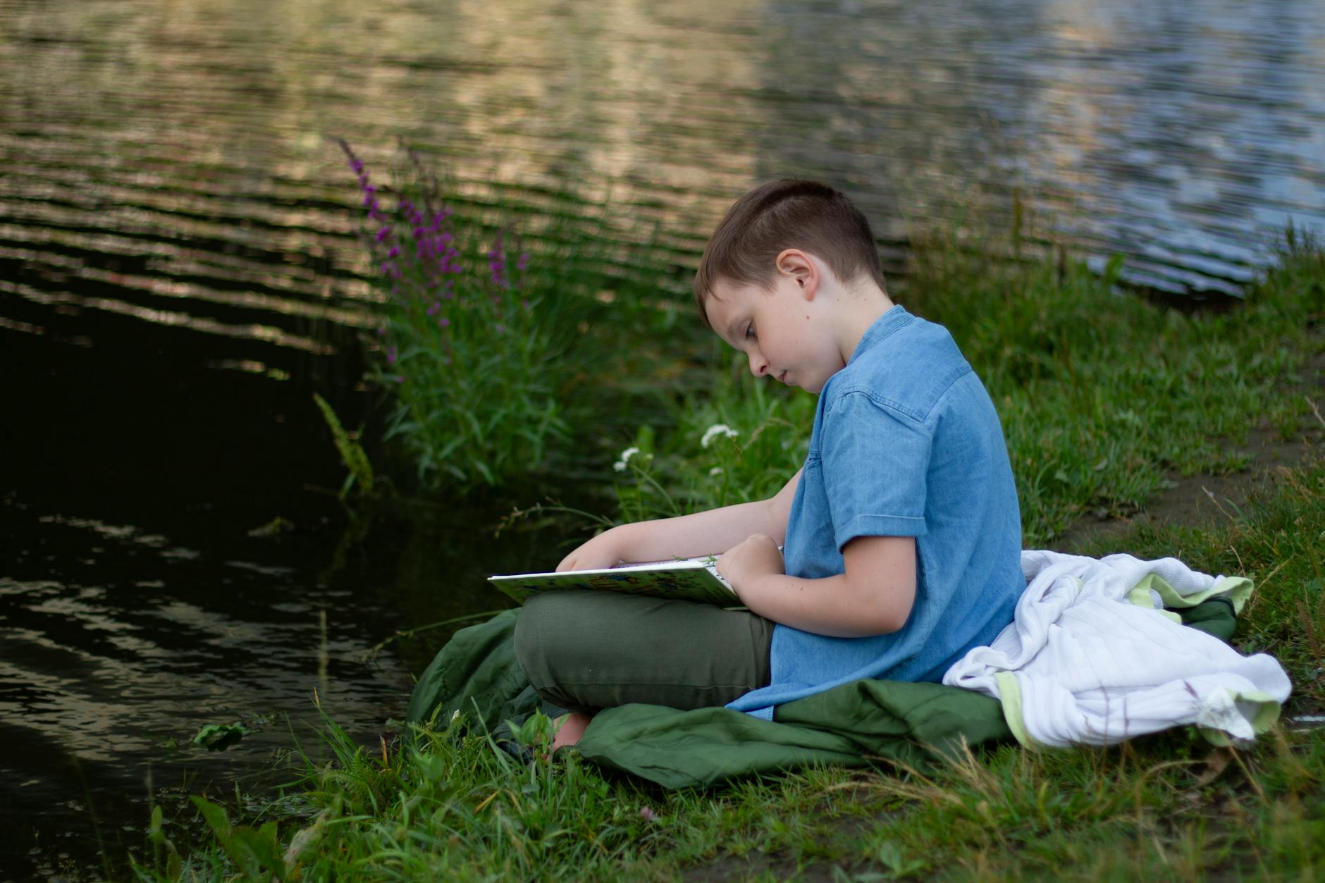 Stock photo of a youngster sitting on a   shore reading from Pexels.com