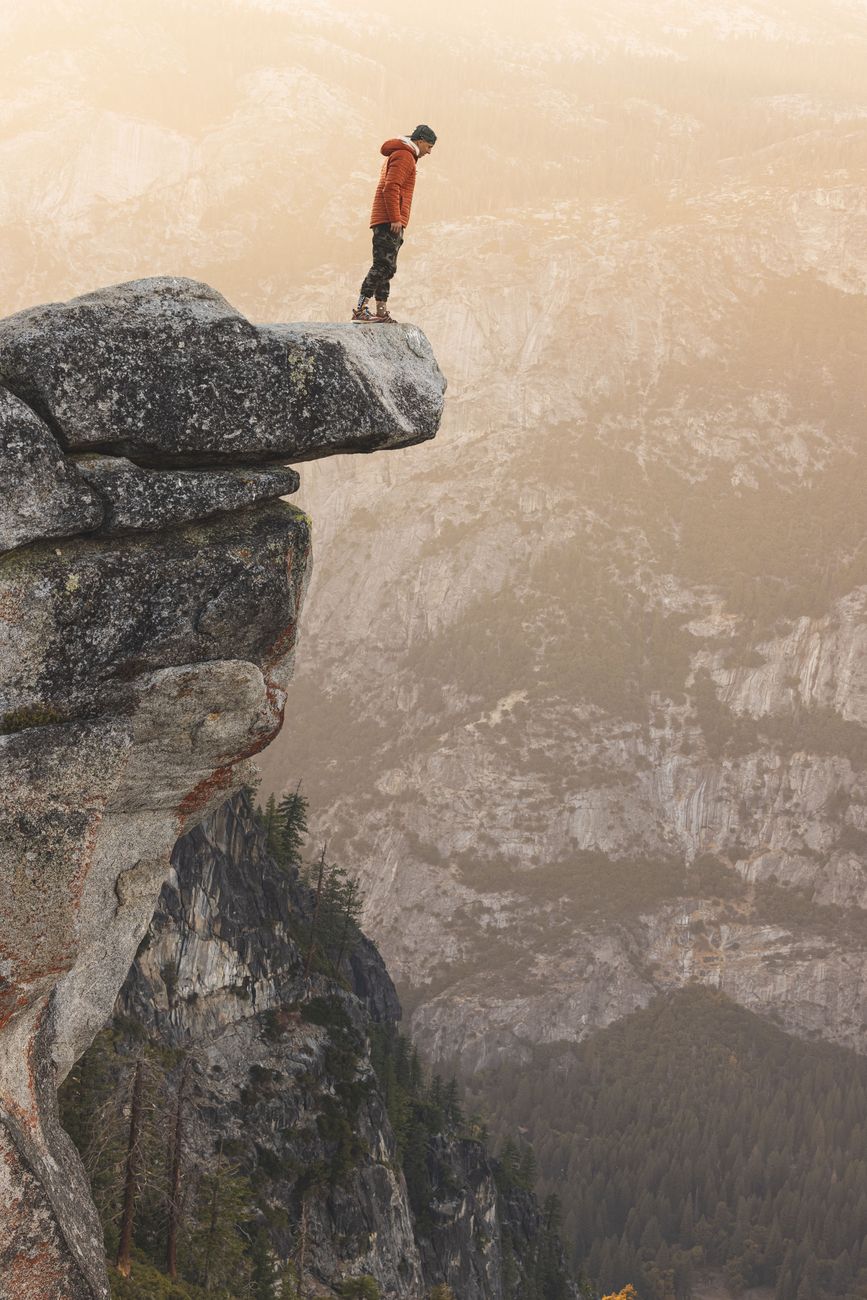 Stock photo of a person looking over the edge standing on a rocky ledge with a long drop ahead from Pexels.com