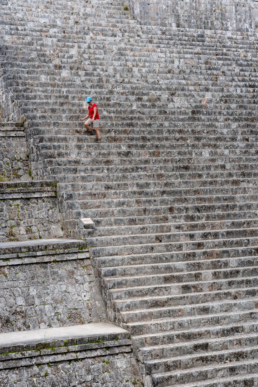 Stock photo of a single small human figure climbing a massive set of stairs outside a mountainous edifice from Pexels.com