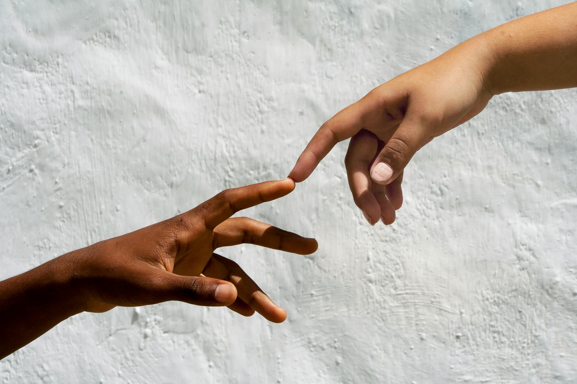 Stock photo of two hands reaching out to touch index fingers over white stucco background from Pexels.com