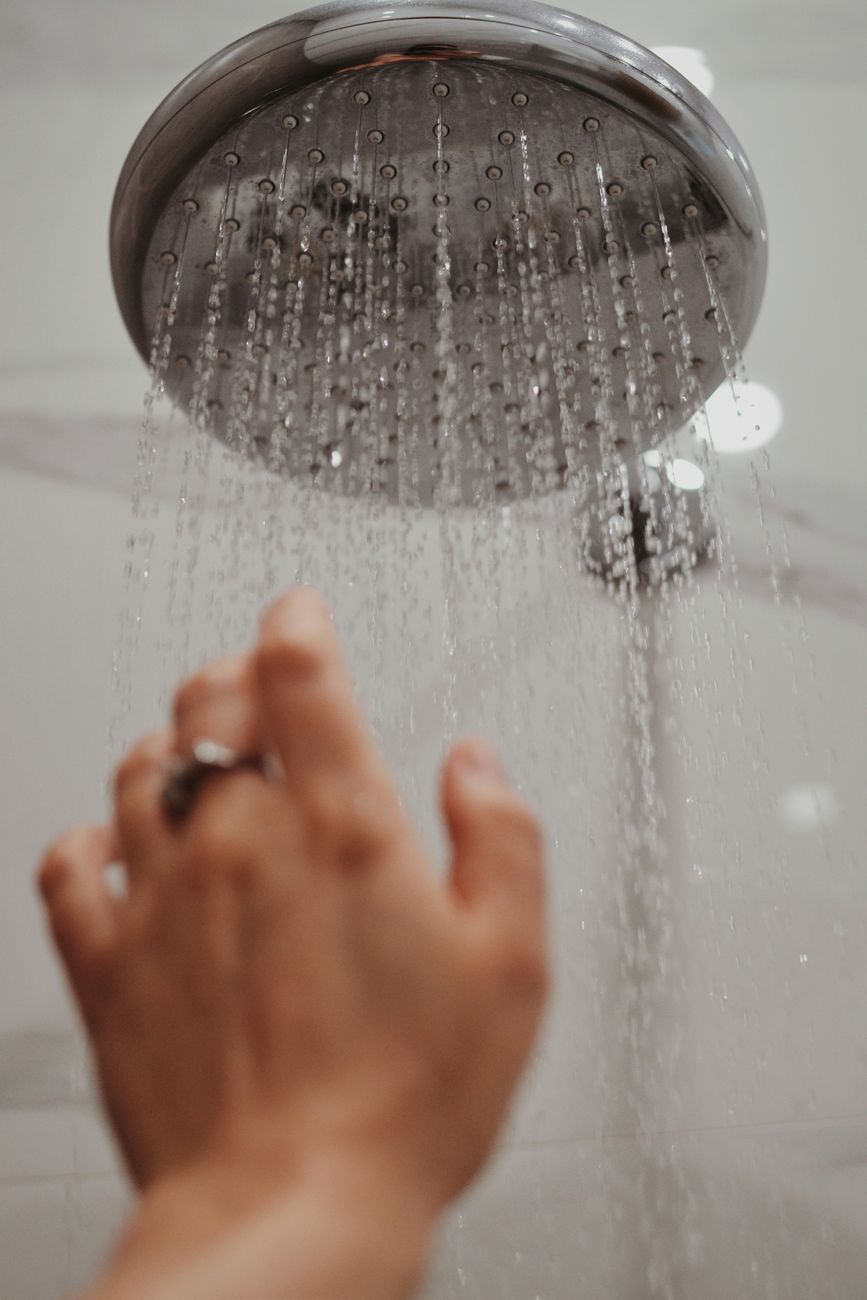 Stock photo or a hand reaching up to adjust a large shower head with streams of water from Pexels.com