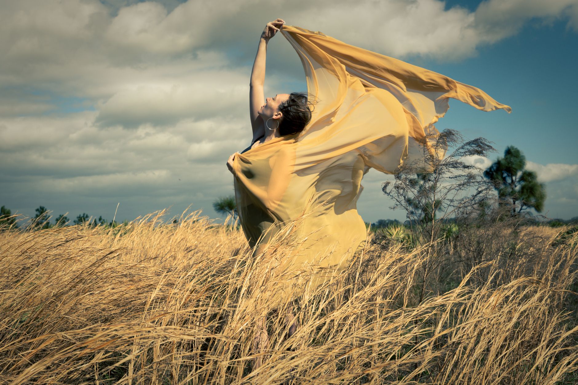 Stock photo of a graceful woman dancing in a sunlit field while holding a billowing sheer yellow shawl from Pexelx.com