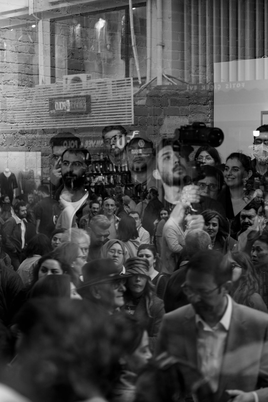 Stock black-and-white image shows a crowd of people gathered in an indoor or covered setting, with various individuals visible from different angles and some motion blur from Pexels.com