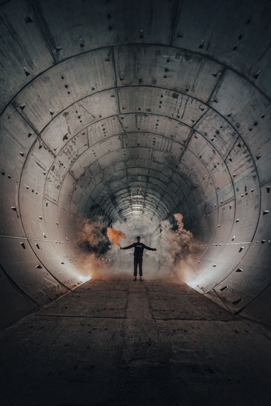 Stock photo silhouette of a person standing inside a large, circular concrete tunnel with smoke flares from Pexels.com