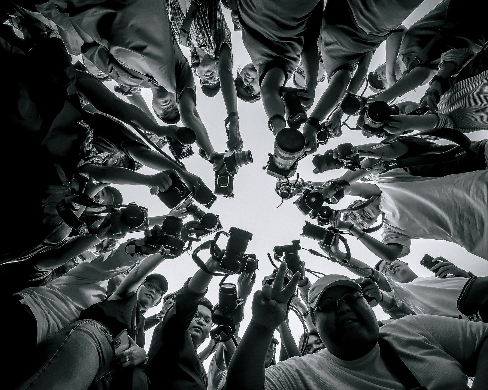 Stock photo a low-angle, black-and-white perspective of a tight circle of photographers and media personnel holding up cameras and lenses toward the center. from Pexels.com