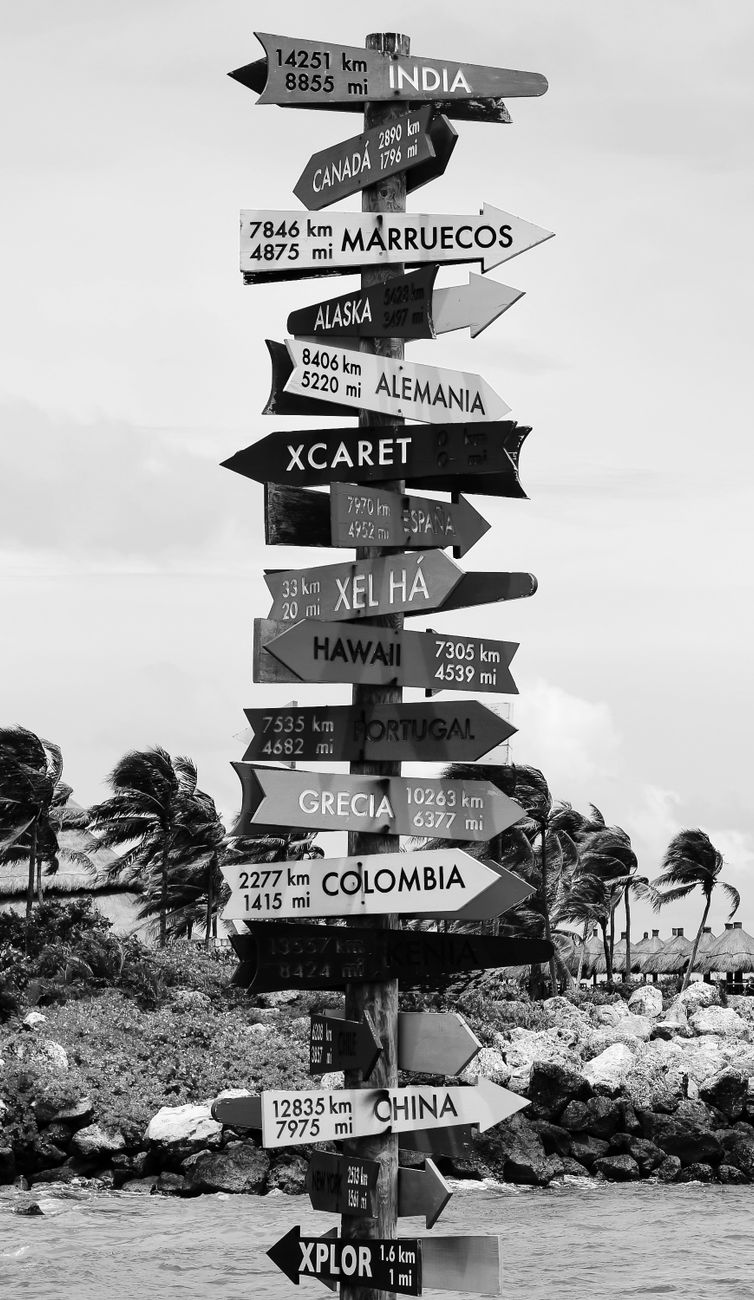 Stock photo shows a black-and-white directional signpost pointing to various global destinations from Pexels