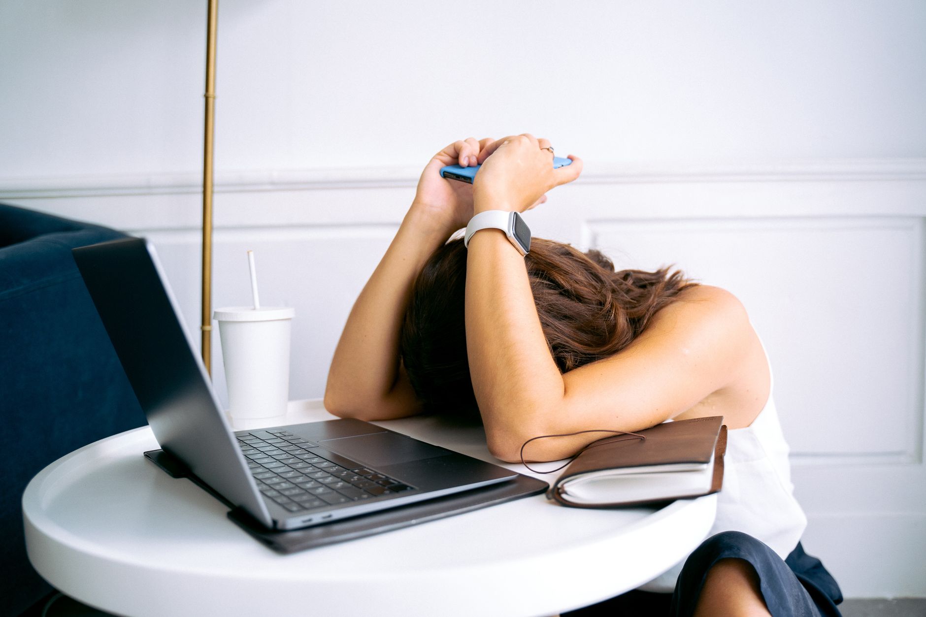 Stock photo of an stressed person resting their head on a table next to a laptop and a drink.from Pexels.com