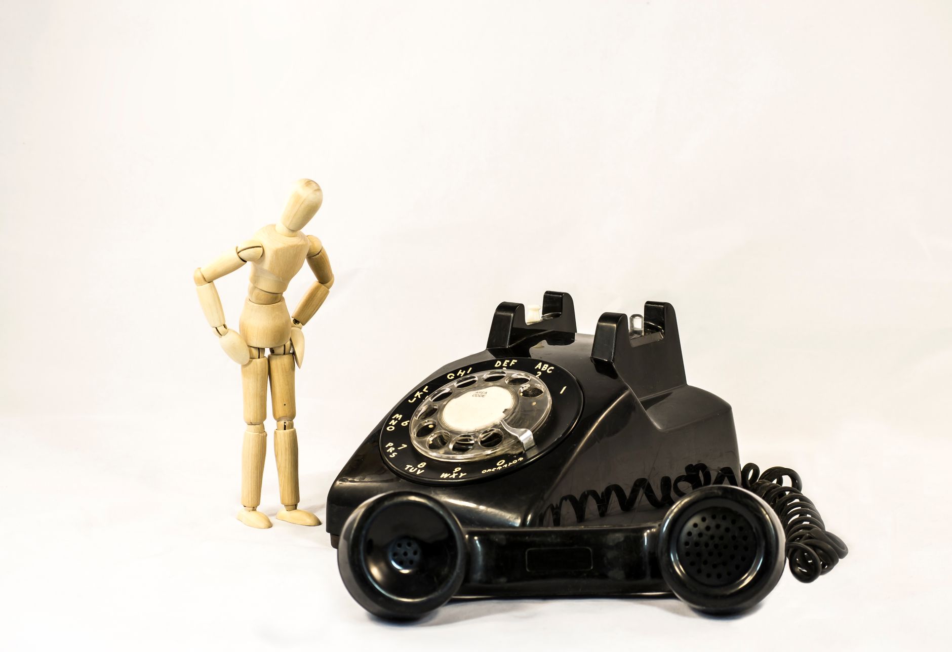 Stock photo of a classic black rotary telephone placed next to a small wooden artist's mannequin from Pexels,com