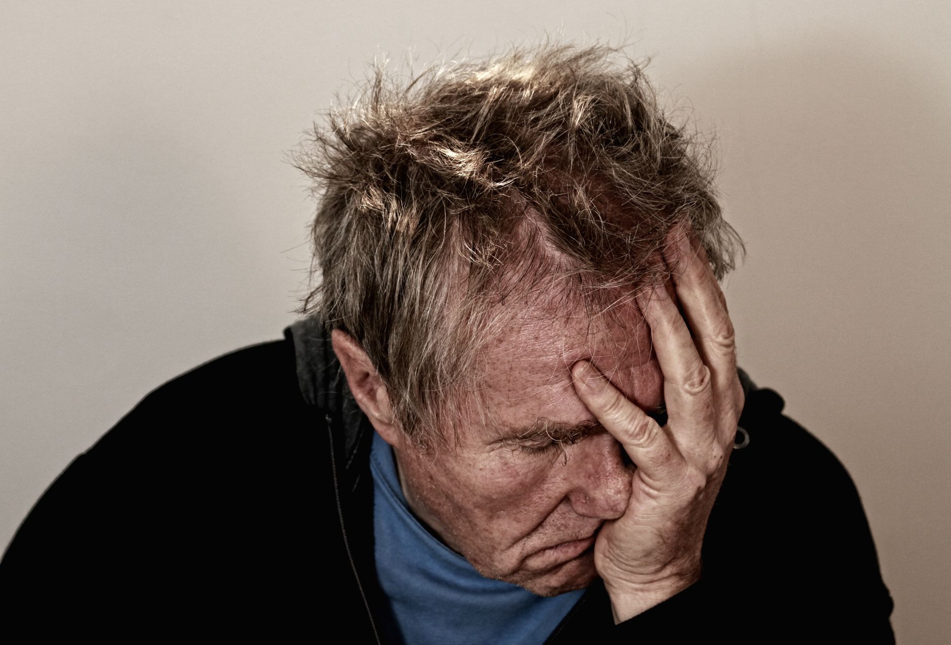  Stock photo of an adult with disheveled hair, wearing a dark outer garment over a blue shirt, with one hand pressed against their forehead and eyes cast downward, which appears to show an expression of deep mental strain, worry, or distress from Pexels.com
