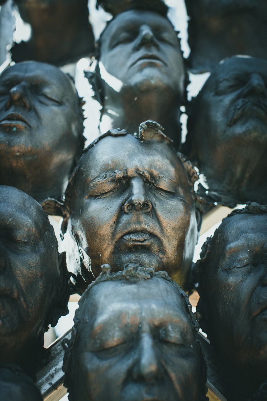 Stock photo close-up photograph of a metallic or dark sculptural installation featuring multiple human faces with closed eyes from Pexels.com
