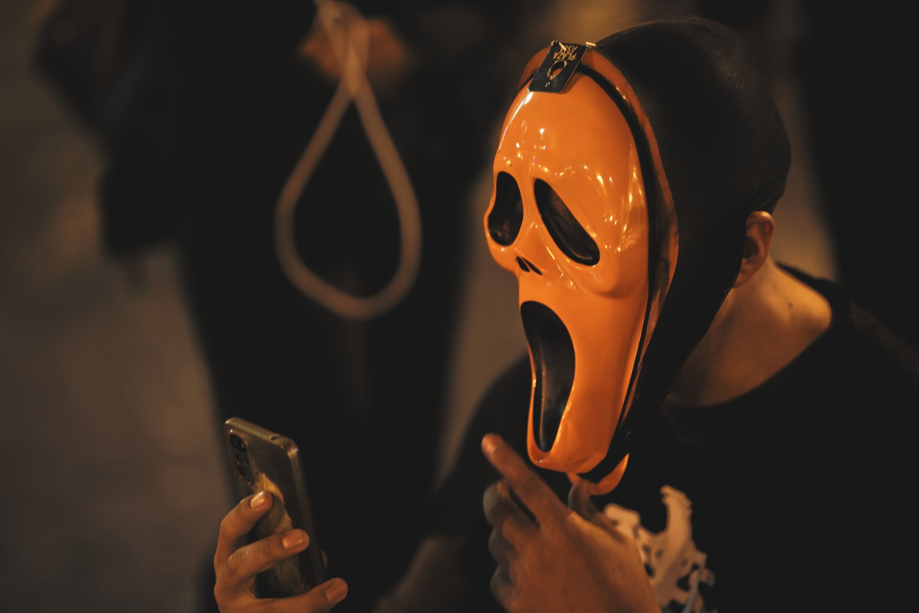 Stock image shows a vibrant orange fluorescent Ghost Face mask scrolling a cell phone from Pexels.com