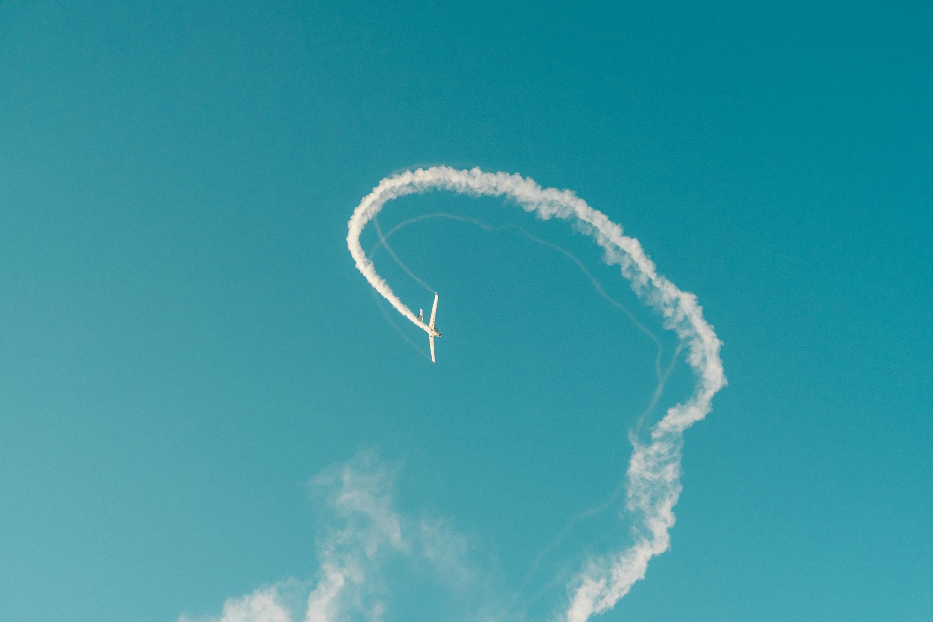 Stock photo shows an aerobatic airplane performing a loop maneuver and leaving a smoke trail against a clear blue sky. from Pexels.com